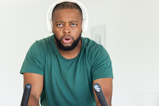 African American man leaning over bike bars, pedaling at home in green tee with white headset