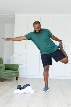 African American man doing standing quad stretch at home wearing green shirt dumbbells towel near