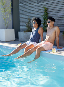 African American male friends sitting poolside, shirtless and navy tank, sunglasses, drinks