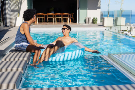 African American men chatting on rooftop pool ledge in swim trunks with inflatable ring