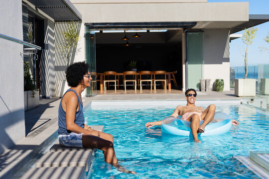 African American men lounging by rooftop pool, one wearing blue tank top, other floating on float