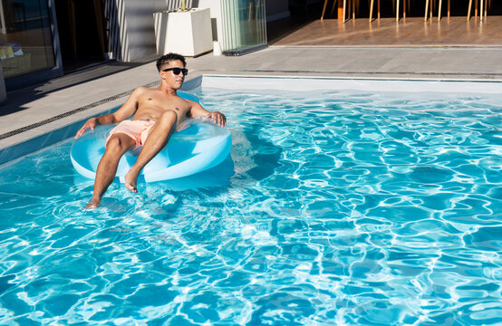 African American man reclining on blue float in pink trunks near pool deck, copy space