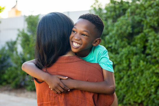 Mother holding African American preteen boy smiling in backyard wearing teal tee and rust top
