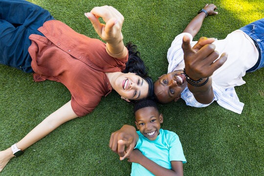 Diverse family lying on bright green grass, smiling and pointing toward camera, showing watches