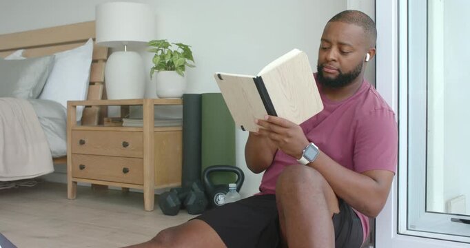 African American man sitting by door in bedroom, rereading notebook, marking with pen to note ideas