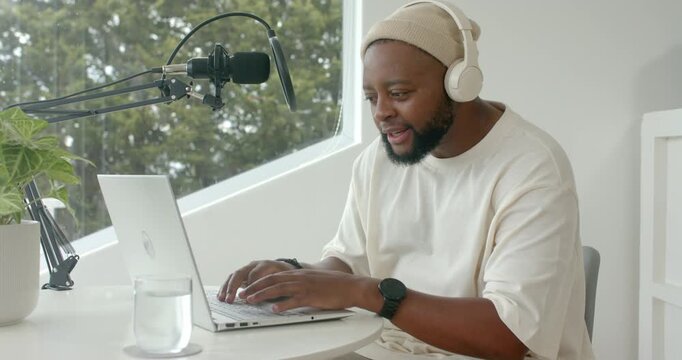 Man wearing headphones starting recording at table typing on laptop and speaking into mic laughing