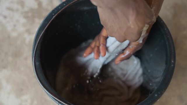 Black bucket hand wash laundry cloth. Close up of hands scrubbing fabric in soapy water, wringing and rinsing with suds and droplets, tactile texture and wet motion, domestic house chore captured