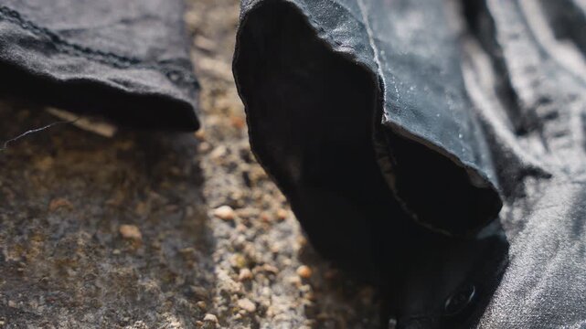 Discarded black sleeve on house doorstep with sand and damp concrete, curled cuff and frayed edge, gritty closeup and moody shadow suggested plot contractor misplacing jacket during renovation