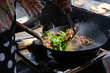 Street vendor cooking thai stir fry in hot wok with fresh basil and ingredients traditional asian cuisine prepared over high heat in outdoor market kitchen creating savory aromatic food © NongEngEng