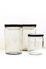 Large and small empty transparent glass bottles with black caps placed on a white table with a clean white background, ideal for cosmetic, pharmaceutical, laboratory or packaging mockup concepts.
