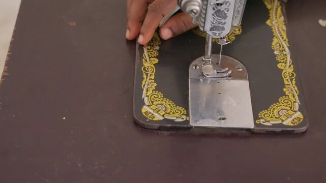 Closeup black hands sewing fabric on vintage machine, yellow decorative trim and steady stitch, focused domestic chore in home workshop, skilled seamstress touch, tactile and intimate atmosphere