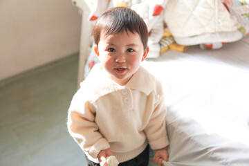 Portrait of a sweet Asian toddler girl standing in a sunlit room. Cute child looking up at camera with innocent smile in natural light at home.