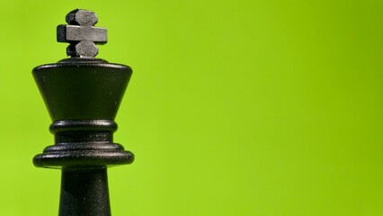 A single black chess king stands prominently against a vibrant green background. This image symbolizes leadership, authority, and strategic isolation in the context of competition and gaming. © FaizAhmad