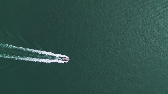 Overhead view footage of a boat sailing across calm blue water on a sunny day, creating ripples and wake patterns from above.