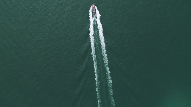 Overhead view footage of a boat sailing across calm blue water on a sunny day, creating ripples and wake patterns from above.