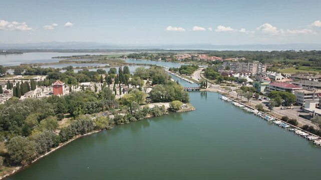 Smooth 4K UHD drone flies forward over the Grado Lagoon toward the central canals, marina and town center with trees and buildings&mdash;ideal for travel films, establishing shots.