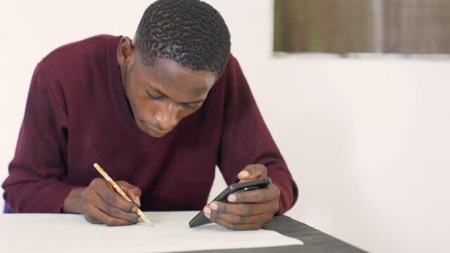 Black male illustrator drawing at table with pencil and phone reference, bright classroom or studio corner, mat on desk, careful precise lines, concentrated posture, commissioned practice