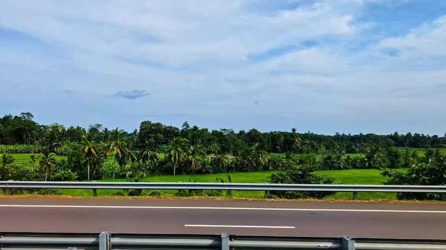 First impression of Sri Lanka landscape near Mattala Rajapaksa International Airport, filmed from a moving car on the highway with lush green fields and tropical vegetation.