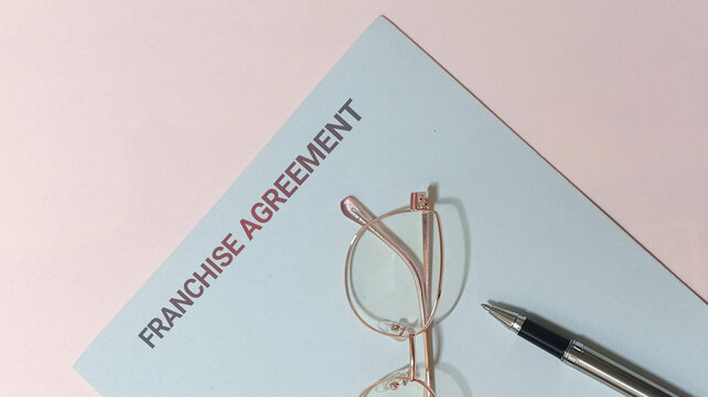 Business contract and legal document for a franchise agreement, depicted with eyeglasses and a pen on a light background, symbolizing partnership, investment, and future collaboration
