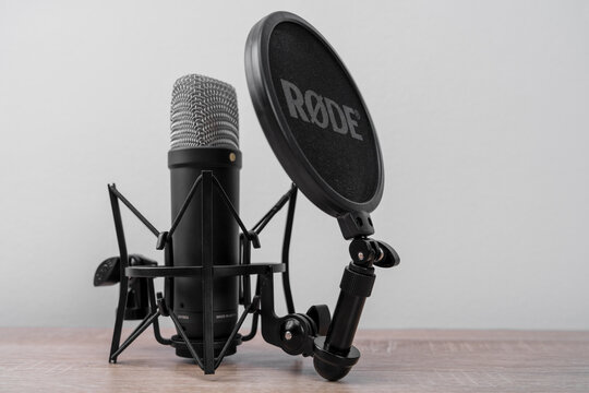 Bar, Montenegro: February 6, 2026: Black studio condenser microphone RODE in shock mount with pop filter on wooden desk against gray wall background, close-up audio recording setup with metal grille