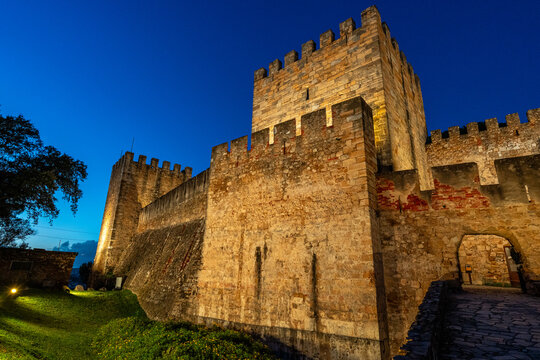 Lisbon, Portugal, the illuminated stone walls and towers of Castelo de S&atilde;o Jorge against a deep blue twilight sky.