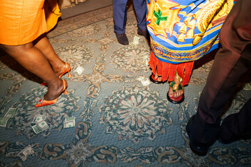 Obraz premium High-angle view of money scattered on a patterned carpet floor during a festive celebration. People's feet in traditional clothing and formal shoes suggest a cultural event or wedding reception, captu