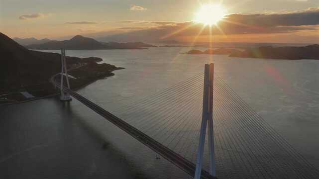 Cinematic drone descent over Tatara Bridge, sun aligning with bridge pylon at sunrise with left copy space.