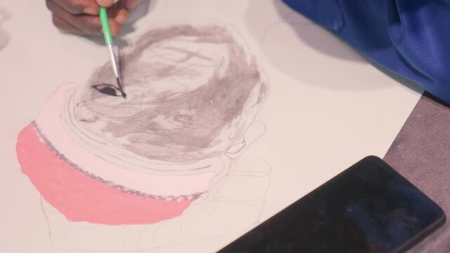 Closeup black painting on canvas showing artist hand applying black wash with brush to circular sketch, pink base layer and smartphone reference on tabletop, textured paper, soft studio light, patient