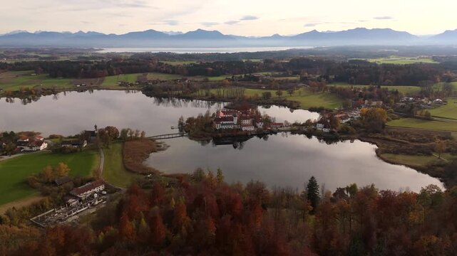Autumn aerial video of Kloster Seeon and St. Nikolaus Chapel in Seeon-Seebruck, surrounded by colorful forests and reflections in lake. Herbstlandschaft Kloster Seeon, barocker Kirche St. Lambert 