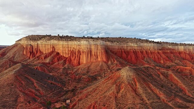View of a vast canyon with high cliffs and dry hills. The ground shows deep colors and textures. Clouds move above the landscape during the evening hours.