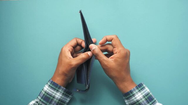 Top view of male hands in a plaid shirt holding and opening an empty wallet on a green surface