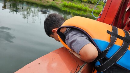 A boys sit on a boat wearing life vest and look at the view around the lake.