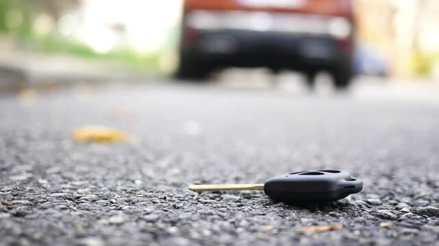 Lost car key on asphalt road with blurred background of vehicle and pedestrian passing by, motion shot