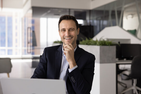 Professional portrait smiling Hispanic male confident executive corporate ceo entrepreneur working on computer at office desk enjoying productive project results motivated for successful career growth