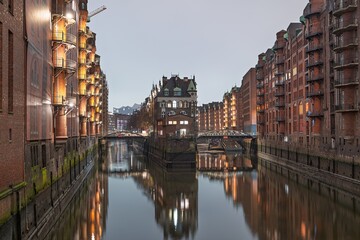 Fototapeta premium Experience the enchanting charm of Hamburg s Speicherstadt at twilight. Its historic warehouses and canal reflections showcase Hamburg s unique architectural beauty and allure.