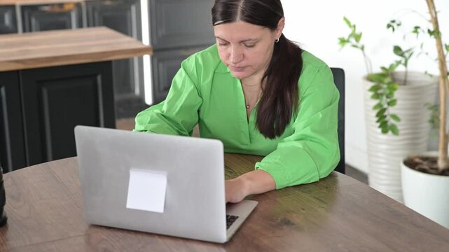 Woman typing on laptop at kitchen table while working from home. Freelance accounting and financial record-keeping concept.