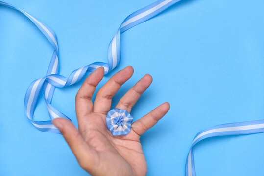 Hand holding an Argentine cockade, escarapela, on a light blue background with a national flag ribbon. Concept: celebration of national holidays.