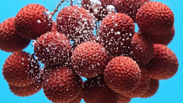 Fresh lychee fruits in effervescent water, their vibrant red skins adorned with sparkling bubbles against a serene blue backdrop, symbolizing pure refreshment and summer joy