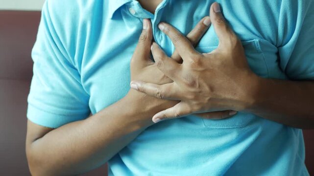 Man experiencing chest pain hands clutching his chest, a clear indication of discomfort or a heart-related issue, cinematic motion footage