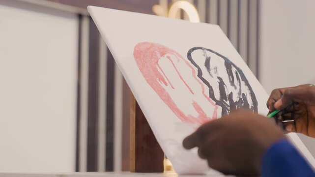 Painter blending shades carefully. Artistic practitioner delicately mixing pink and black paints. Creative professional meticulously refining heartfelt artwork using gentle brush strokes indoors