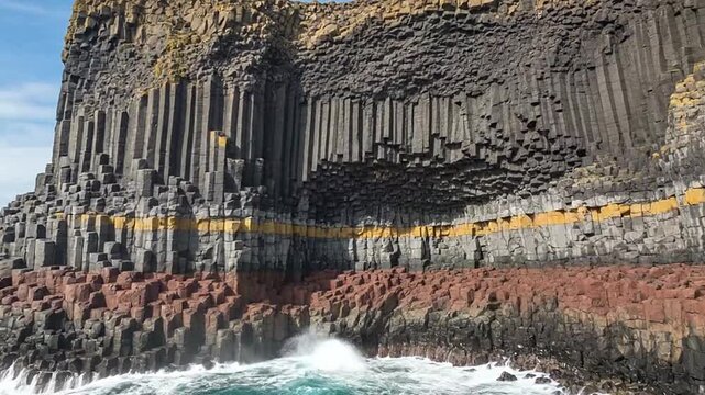 Impressive coastal rock formations with distinctive basalt columns and layered geological strata, with ocean waves crashing below.
