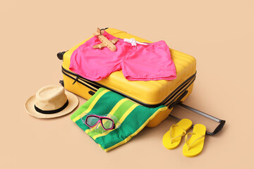 Suitcase with swimming trunks and beach accessories on beige background