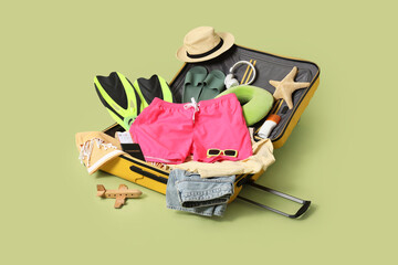 Suitcase with swimming trunks and travel accessories on green background © Pixel-Shot