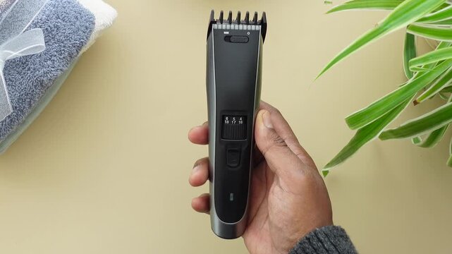 Close up of hand adjusting beard trimmer length settings with comb attachment on towel and plant