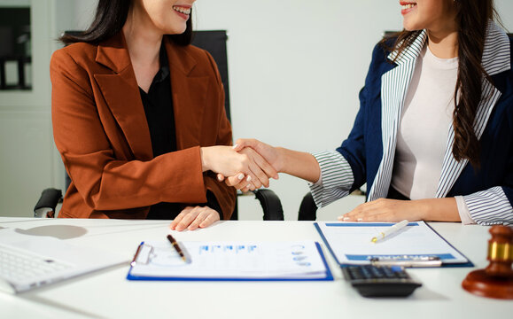 Woman lawyer hand and women client shaking hand collaborate on working agreements with contract documents