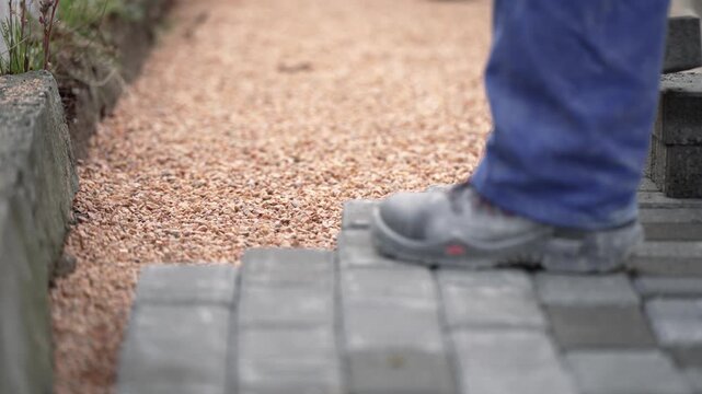 The master in yellow gloves lays paving stones in layers on sidewalk construction site, slow motion