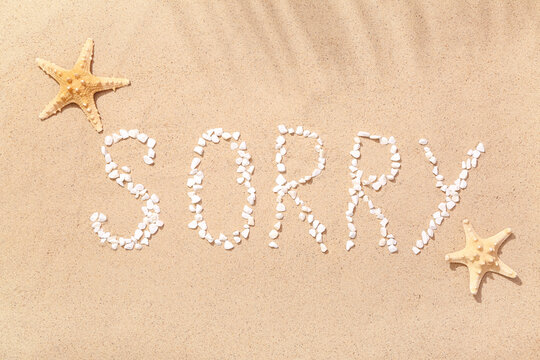 Word SORRY made of pebbles with starfishes on sand