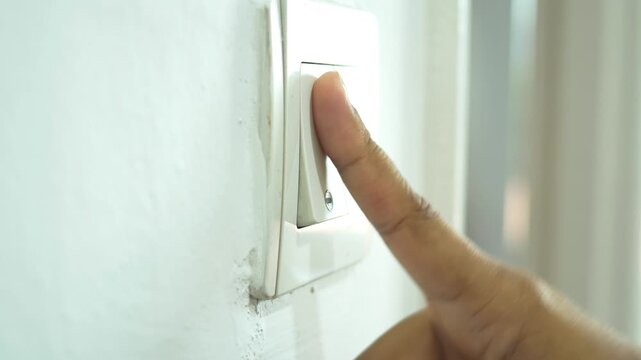 Close up of finger pressing white light switch on wall to turn off or on illumination in room