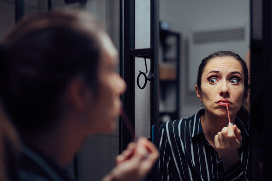 Stressed Woman Messing Up Lipstick Application While Looking In Mirror. Frustrated woman accidentally smudging her red lip gloss while checking her reflection indoors 
