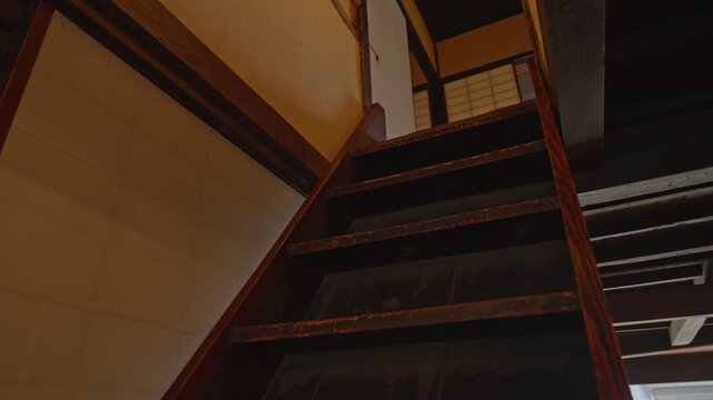A low-angle shot of a narrow and steep dark wood staircase, showcasing the minimalist and functional architecture of a nostalgic Showa-era interior.
